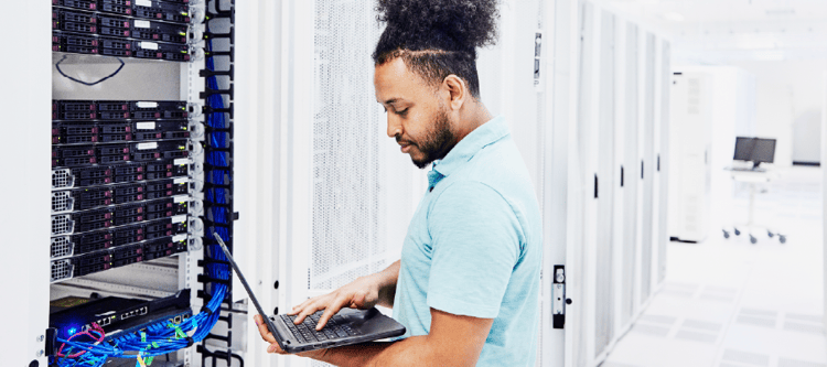Homem trabalhando em um servidor, monitorando sistemas com um laptop em um ambiente tecnológico e moderno, otimização de servidores.