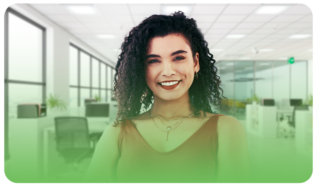 Mulher de cabelos cacheados sorrindo para a câmera com o escritório ao fundo